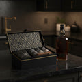 a glass and stones in a decorative box next to a bottle of whisky