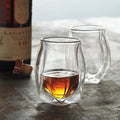 Two glass tumblers with a drink, one filled, on a textured surface with a bottle in the background.