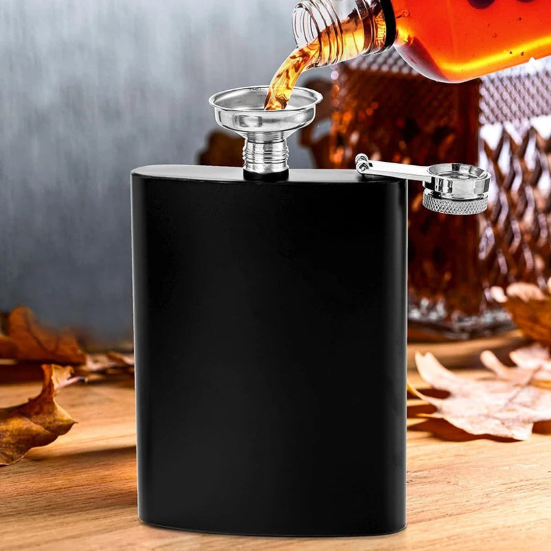 Black hip flask with a bottle pouring liquid into it on a wooden surface.