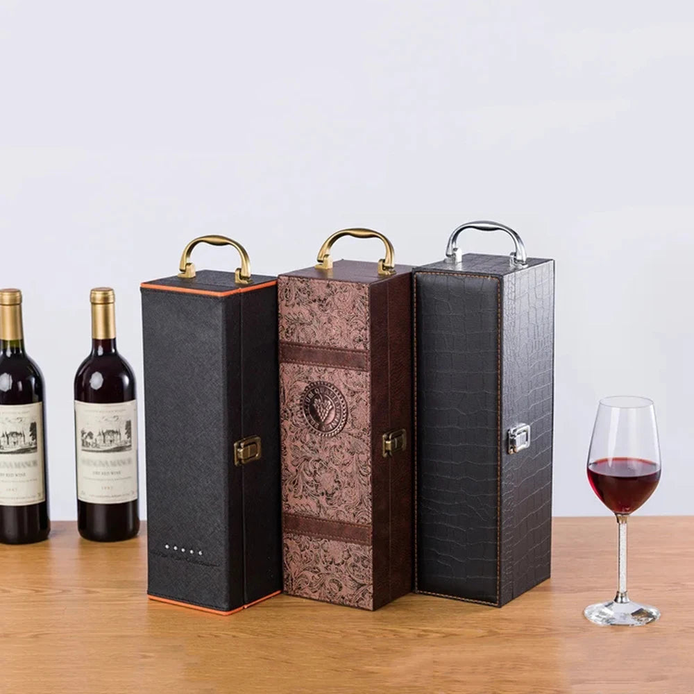 Three wine boxes of different designs on a wooden surface with two wine bottles and a glass of red wine.
