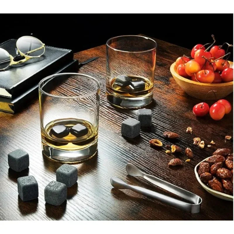 Two glasses of whiskey with stones on a wooden table, surrounded by cherries and nuts.