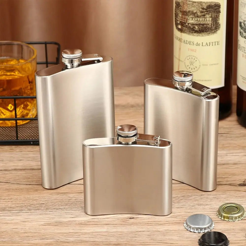 Three metallic flasks on a wooden surface with bottles and glasses in the background.