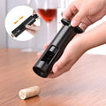 Person using a black wine opener on a cork with a blurred glass of red wine in the background.