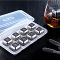 Set of metal ice cubes in a clear plastic container with a glass of whiskey on a dark surface.