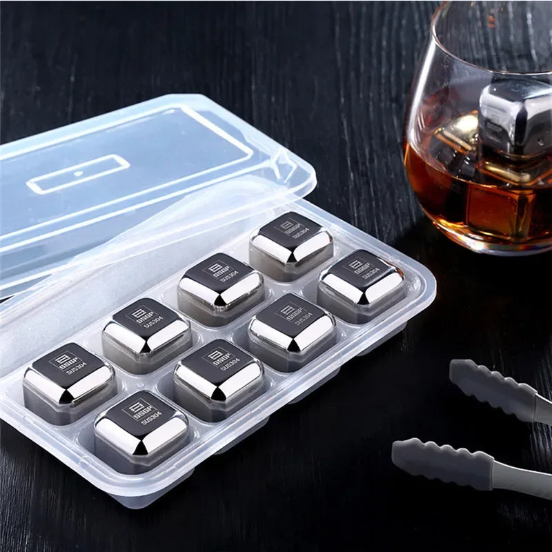Set of metal ice cubes in a clear plastic container with a glass of whiskey on a dark surface.