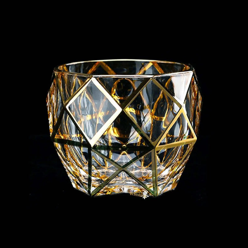Clear glass candle holder with gold geometric patterns on a black background