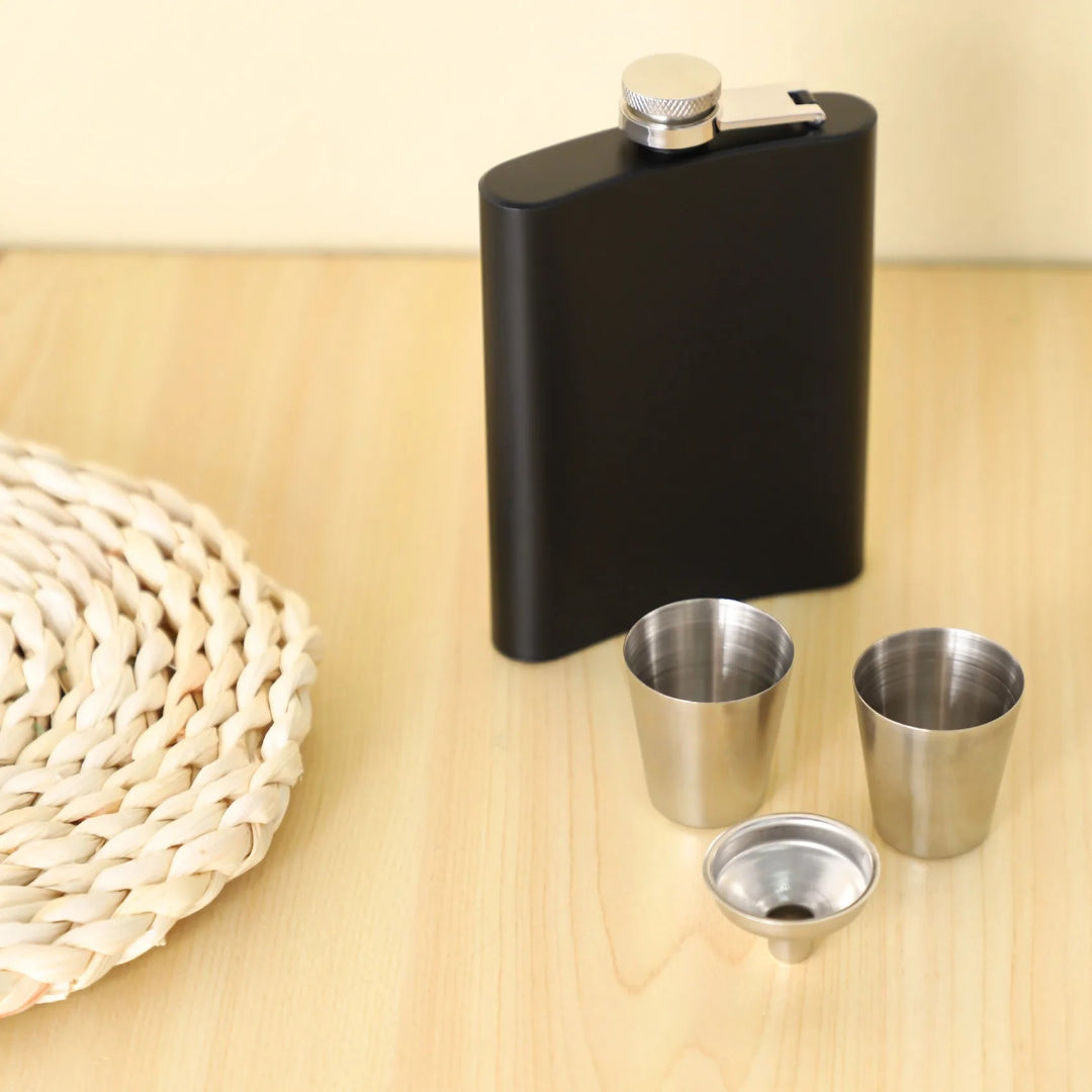 Black flask with three silver shot glasses on a wooden surface